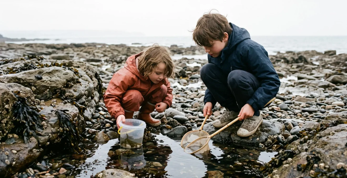 Two children explore a tidal rock pool with nets and a bucket on a stony beach.